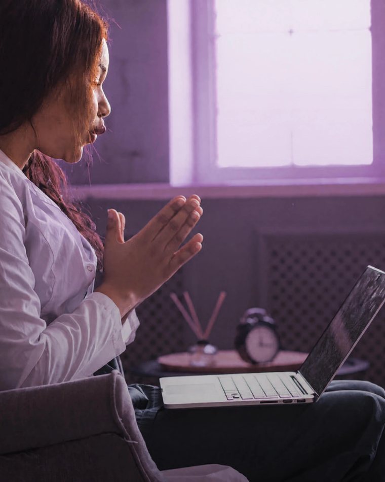 A woman at home talking on a video call, a laptop resting on her lap